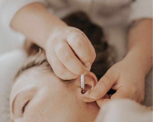 Vyöhyketerapeuttinen synnytyksen käynnistyshoito Porvoossa – hoitajan kädet painelee heijastepisteitä korvassa